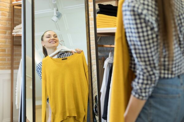 chica se mira en el espejo con un jersey tono ocre